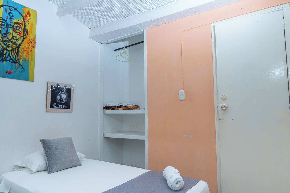 A bedroom with a bed, a wardrobe, a hanging rack, and a painting on the wall.