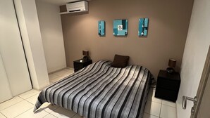 Un dormitorio con una cama grande, dos mesitas de noche, un aire acondicionado instalado en la pared y tres obras de arte en la pared.