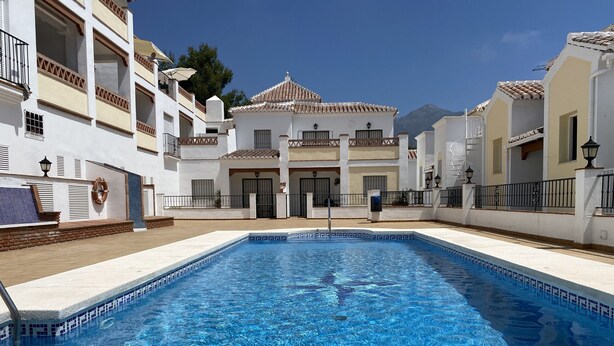 A swimming pool surrounded by white buildings with balconies, a clear sky, and mountains in the background. - Chimenea Pinar 2 Apartment by Casasol (Nerja)