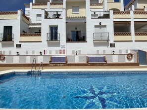A swimming pool with a starfish mosaic design, surrounded by a white building with balconies and windows. - Chimenea Pinar 2 Apartment by Casasol (Nerja)