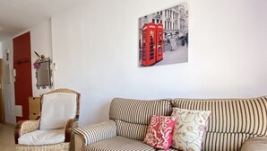 A living room with a striped sofa, a wicker chair, and a glass coffee table. - Chimenea Pinar 2 Apartment by Casasol (Nerja)