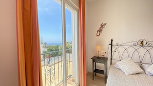 A bedroom with a bed, a nightstand, a lamp, and a view of the sea through a sliding glass door. - Chimenea Pinar 2 Apartment by Casasol (Nerja)