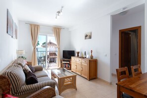 Un salon comprenant un canapé, une table basse en verre, un meuble pour la télévision et un coin repas avec une table et des chaises en bois.