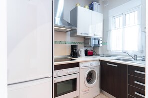 Une cuisine compacte équipée d’un four encastré, d’un four à micro-ondes et d’un lave-linge.