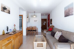 Una sala de estar con un sofá, una mesa de comedor con sillas, una zona de cocina con armarios, y un pasillo que lleva a otra habitación.