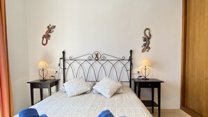 A neatly made bed with pillows and blue towels, two bedside tables with lamps, and decorative wall hangings. - Chimenea Pinar 2 Apartment by Casasol (Nerja)