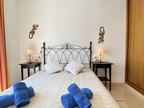 Un lit bien fait, agrémenté d’oreillers et de serviettes bleues, deux tables de chevet avec des lampes et des éléments décoratifs accrochés au mur.