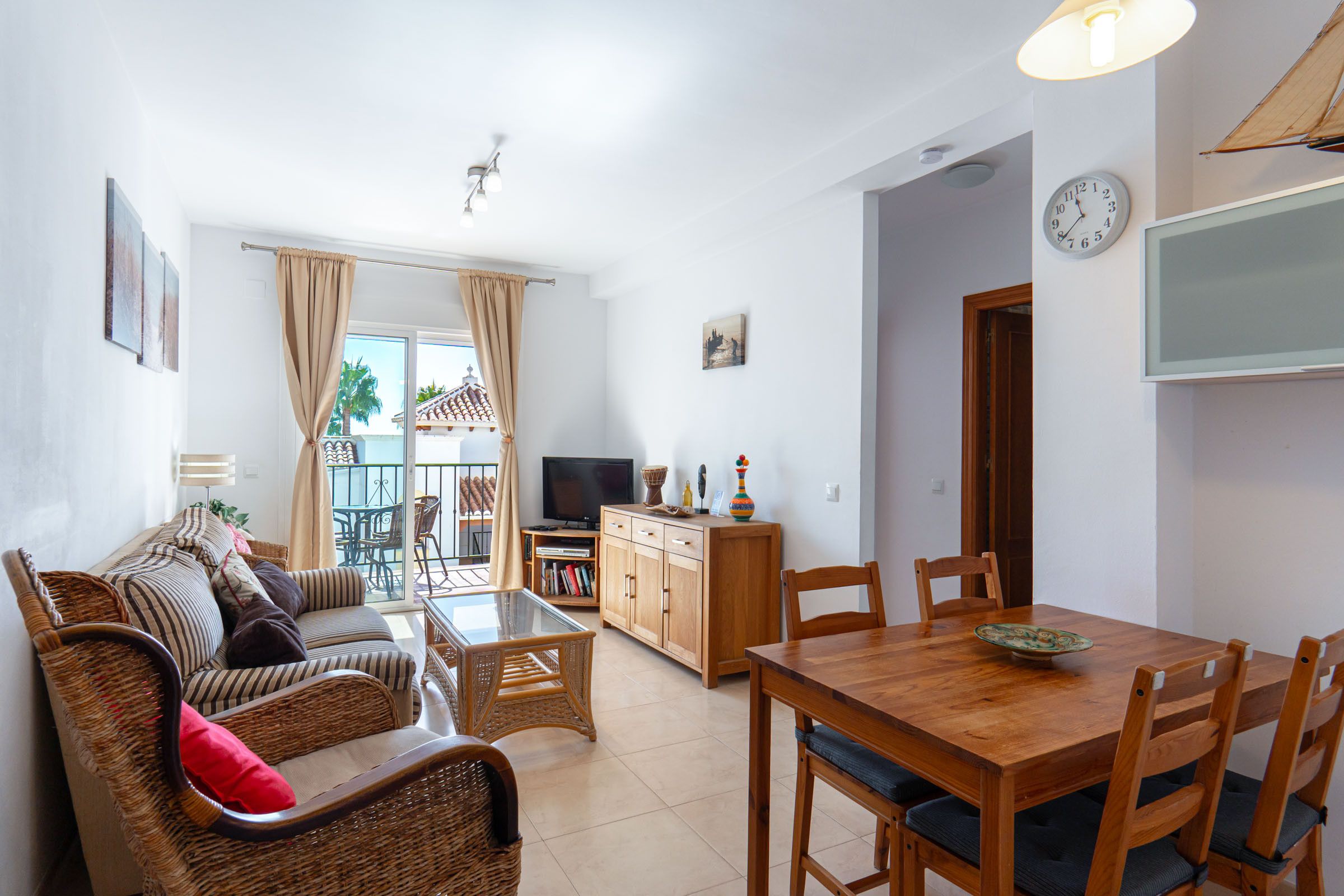 A living room with a sofa, a dining table with chairs, a TV, and a balcony with a view.