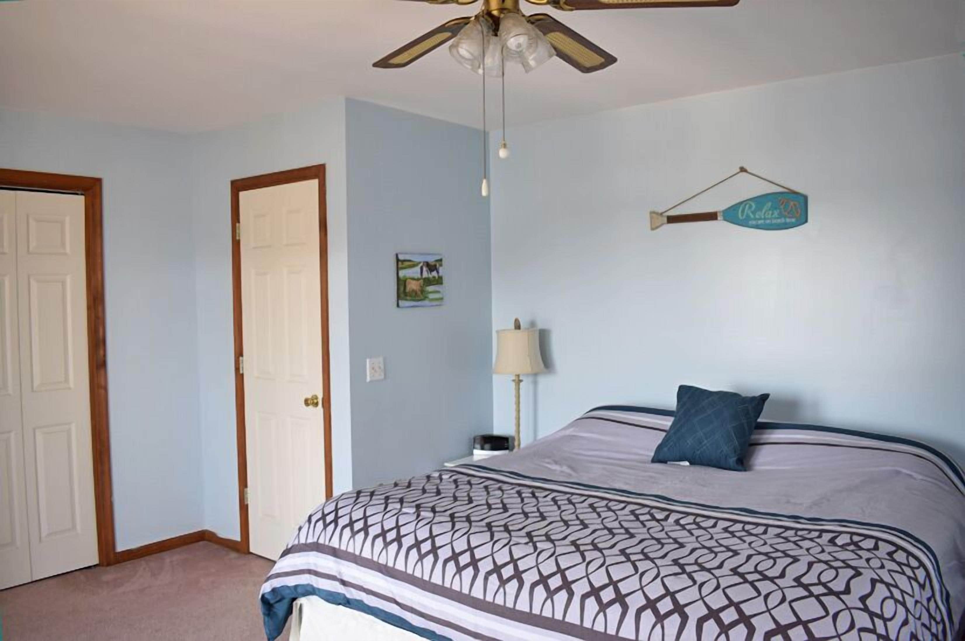 A bedroom with a bed, a ceiling fan, a wall-mounted lamp, and a door.
