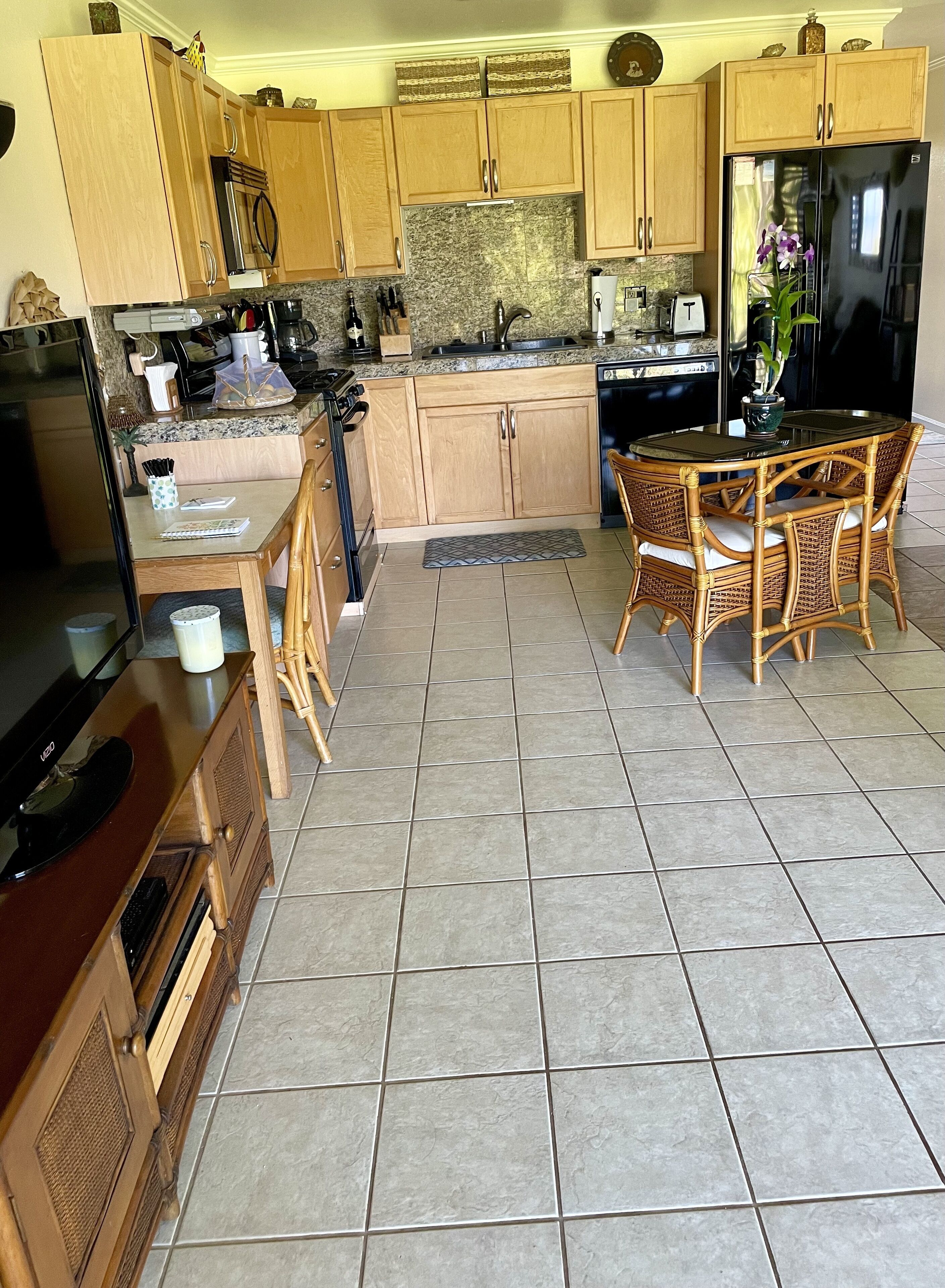 A kitchen with wooden cabinets, a granite countertop, a dining table with wicker chairs, and a black refrigerator.