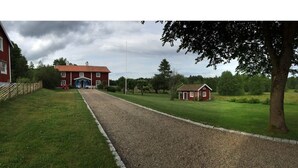 Sorapäällysteinen ajotie johtaa punaiseen rakennukseen, jonka sisäänkäynti on sininen. Rakennuksen ympärillä on vihreää ruohoa ja puita.
