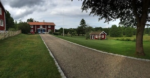 A gravel driveway leading to a red building with a blue entrance, surrounded by green grass and trees. - Gräshult, Justusbo (Skillingaryd)