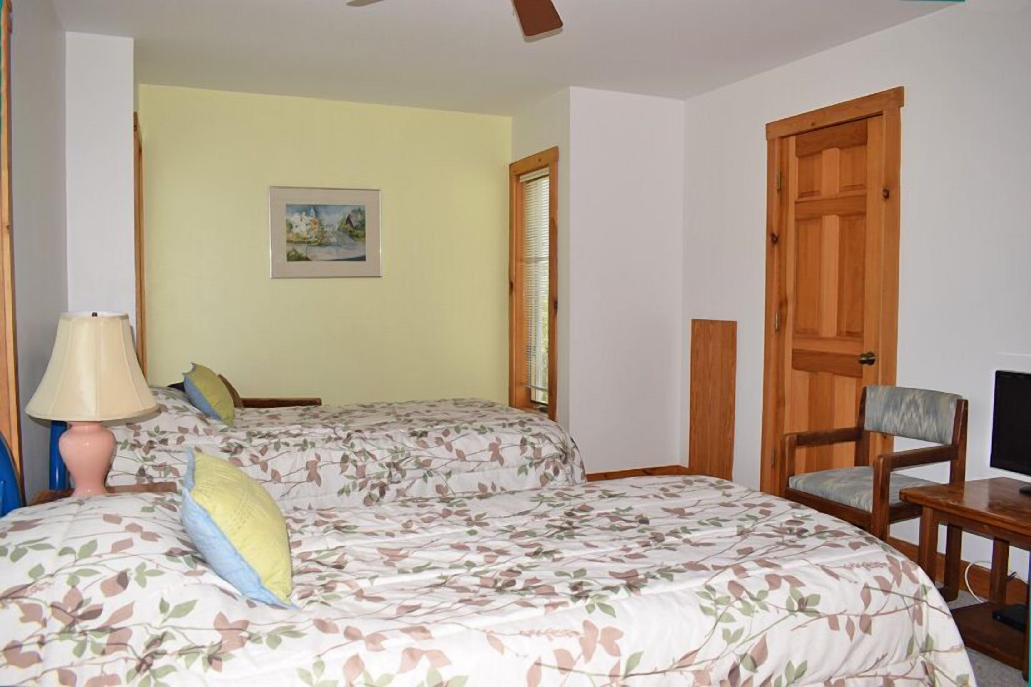 A bedroom with two beds, a desk, a chair, a lamp, and a painting on the wall.