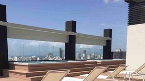 Un área de lounge en la azotea con sillones solarium y vistas al horizonte de la ciudad.