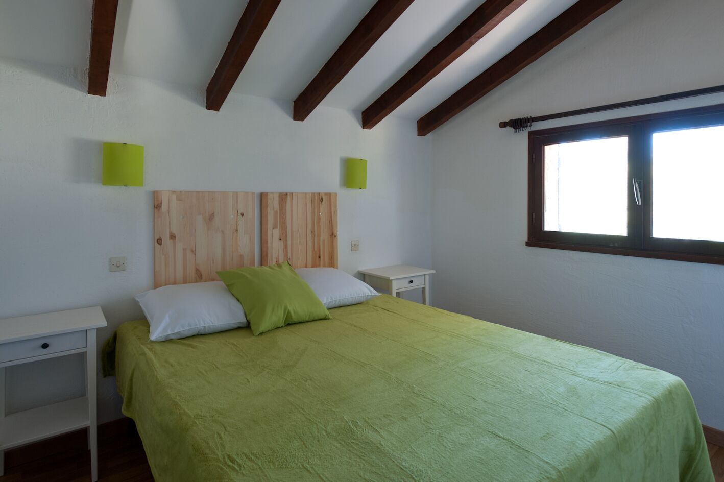 Ein Schlafzimmer mit einem Holz-Kopfteil, einer grünen Bettdecke, zwei Nachttischen und einem Fenster mit Blick.
