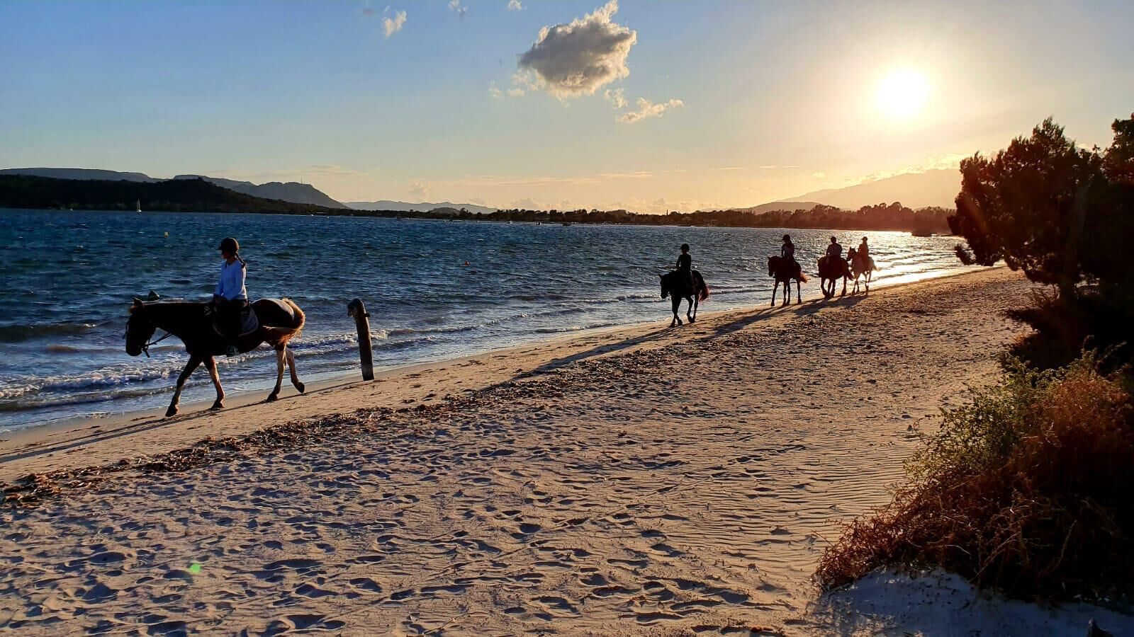 Een strand met een pad voor paardrijden, een wateroppervlak en heuvels in de verte.