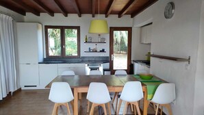 Una cocina moderna con armarios blancos, una mesa de comedor de madera con cuatro sillas, una lámpara colgante amarilla y un reloj en la pared.