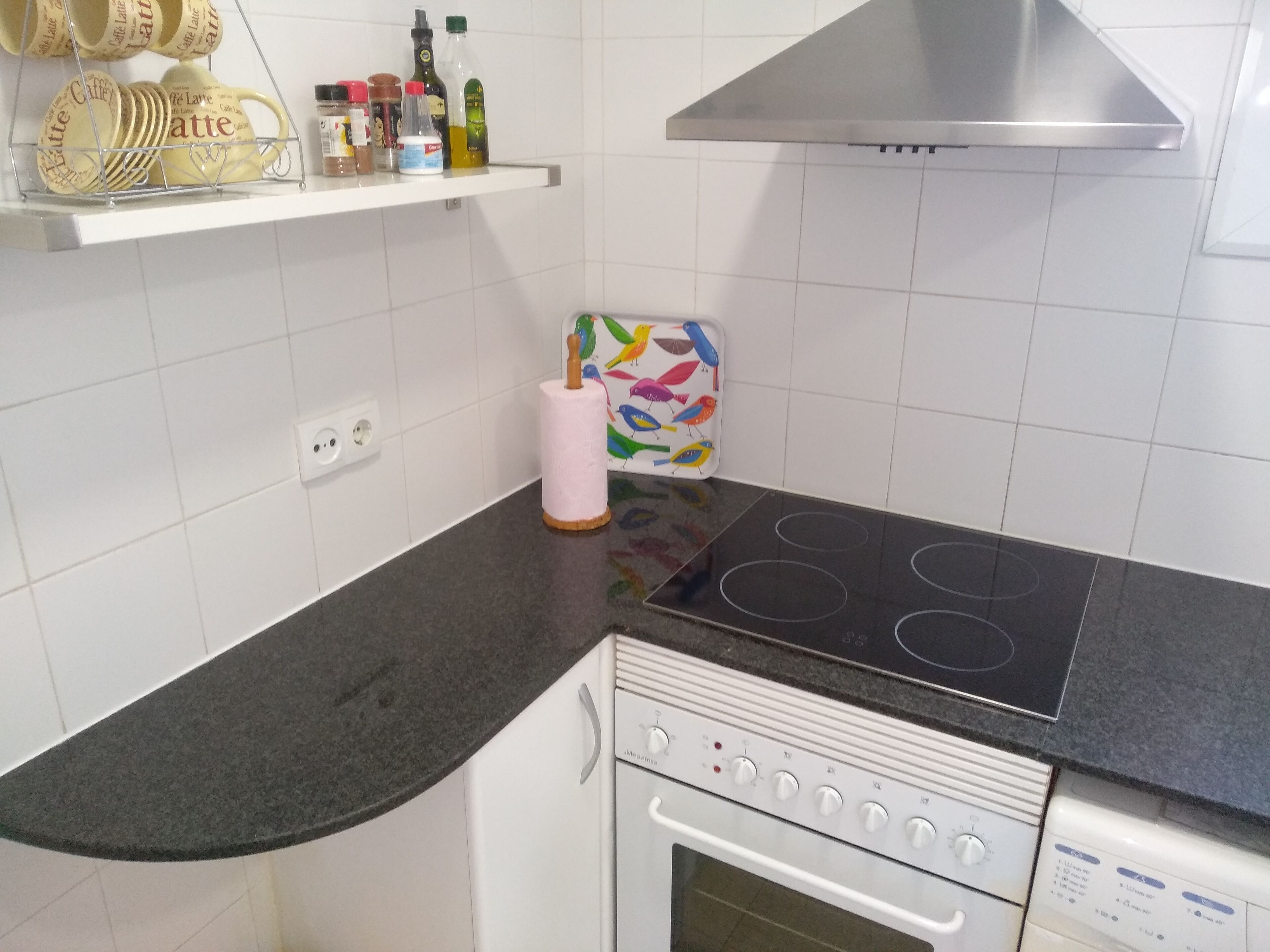 Een keuken met een zwart aanrecht, witte kasten, een rvs afzuigkap en een inbouwoven.