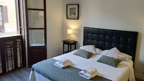 Un lit bien fait, avec une tête de lit sombre, une table de chevet sur laquelle se trouve une lampe, et un tableau encadré accroché au mur.