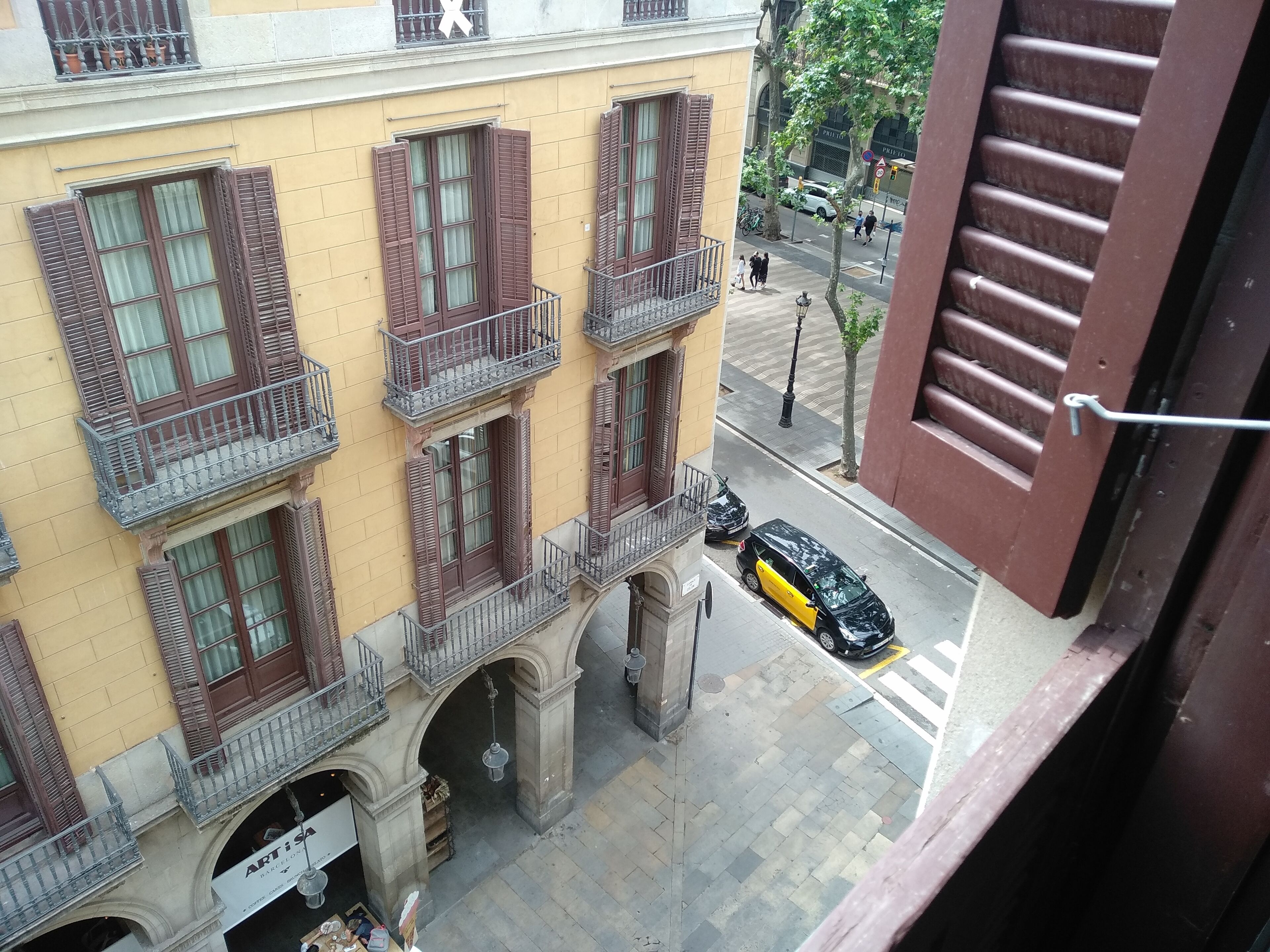 A yellow building with brown shutters and balconies, a street with cars, and a pedestrian crossing.