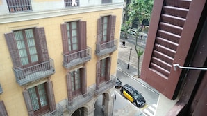 Un bâtiment jaune avec des volets et des balcons bruns, une rue avec des voitures et un passage piéton.