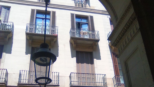 Un immeuble doté de nombreux balcons, une enseigne indiquant « SOUVENS REIAL » et un panneau en forme de « D » signalant un commerce.