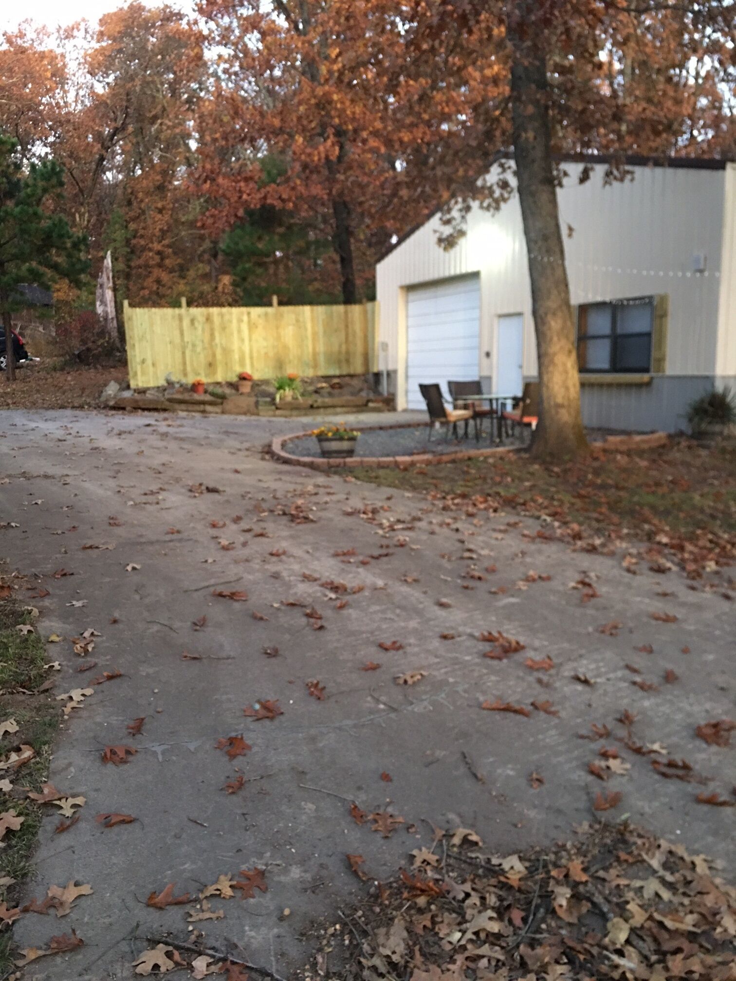 Une allée menant à une maison, avec un garage, une clôture en bois et un arbre.