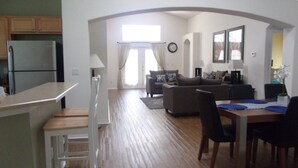 Une cuisine moderne équipée d’un réfrigérateur, un coin repas avec une table et des chaises, et un salon avec un canapé et une table basse.