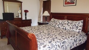 Une chambre à coucher avec un lit en bois, une commode, un miroir, une lampe et un tableau accroché au mur.