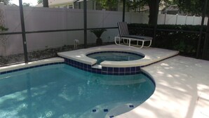 Une piscine avec un jacuzzi, entourée d’une clôture blanche et agrémentée d’une chaise longue.