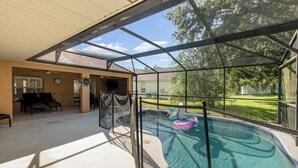 En pool utomhus med tak, med utsikt över en trädgård, ett uteområde med möbler och en grillplats.