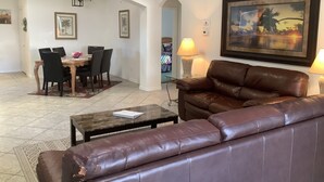 A living room with a brown leather sofa, a dining table with chairs, a coffee table, and a painting on the wall.