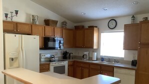 A kitchen with wooden cabinets, a microwave, stove, sink, and a clock on the wall.