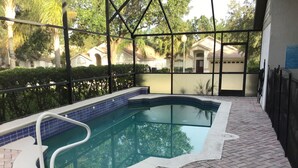 A swimming pool with a tiled edge, surrounded by a brick patio and a metal fence.