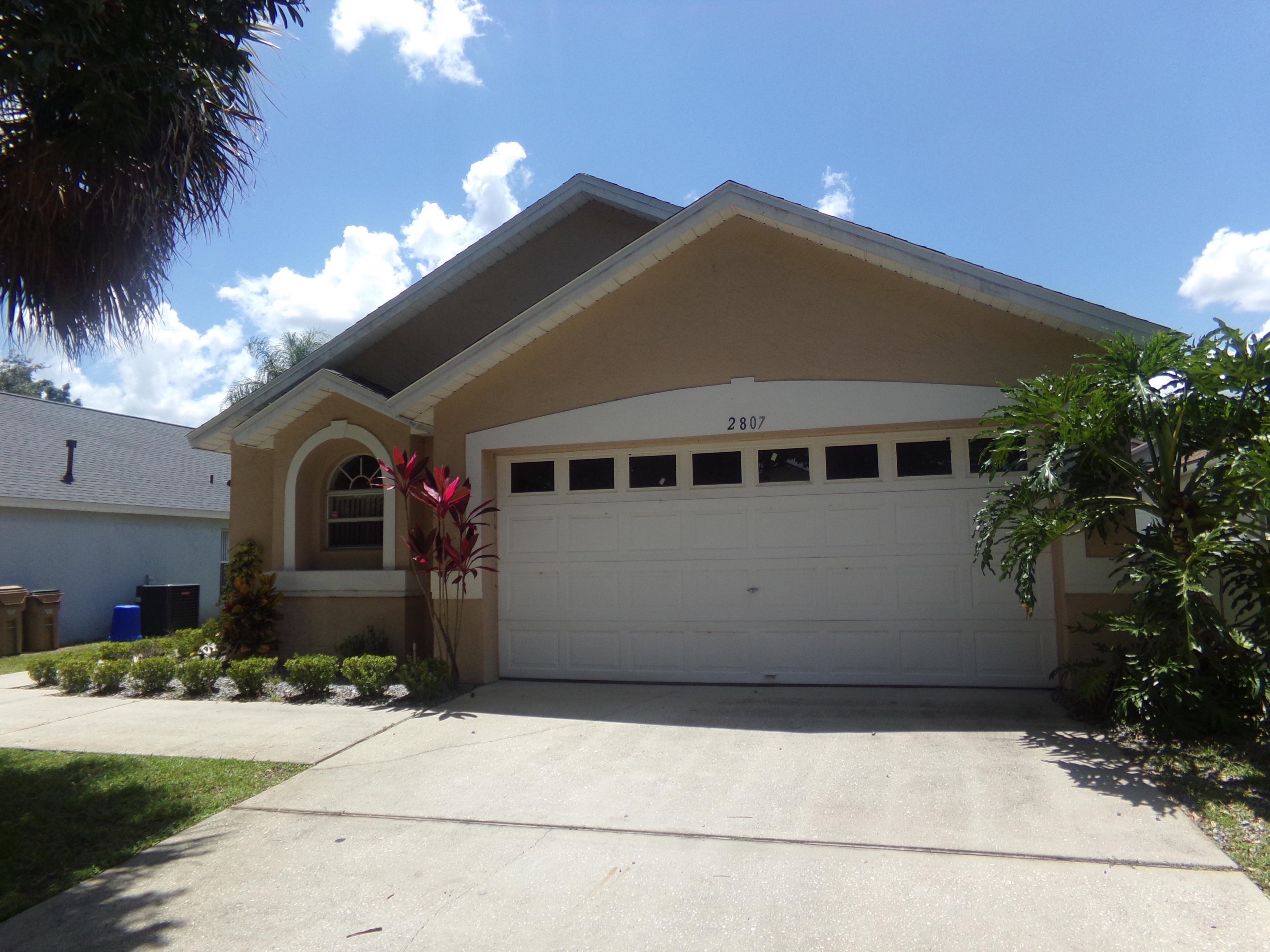 A residential house with a beige exterior, a white garage door, and a number 2807 on the roof.