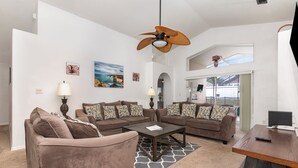 Ein geräumiges Wohnzimmer mit einem Ecksofa, einem Couchtisch und einem Deckenventilator.