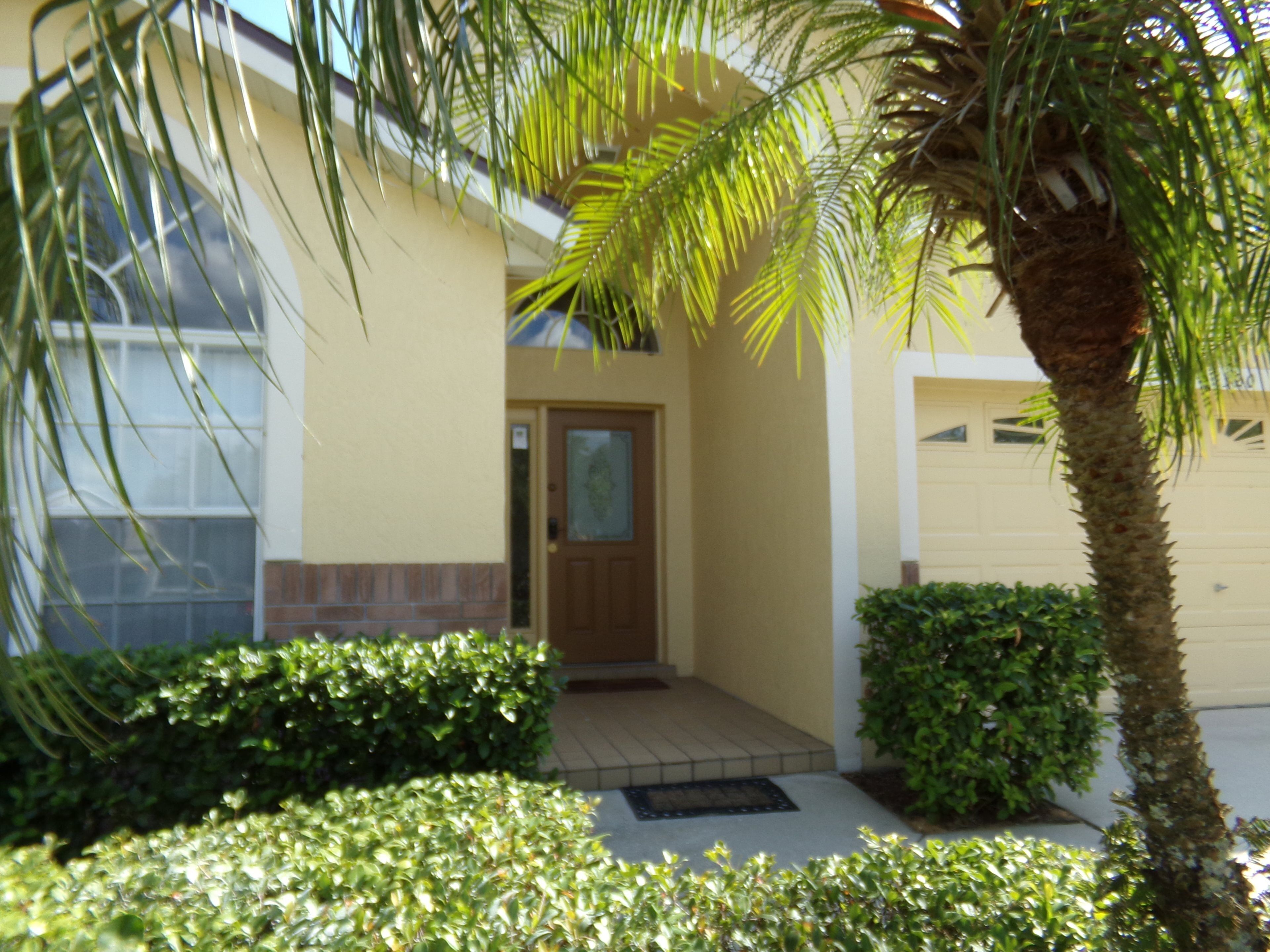 A residential building with a front door, a small porch, and a palm tree.