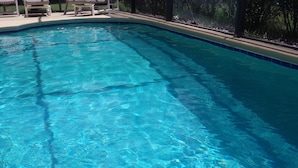 Ein klarer Pool mit einer gefliesten Kante und einer Holzterrasse mit Stühlen.