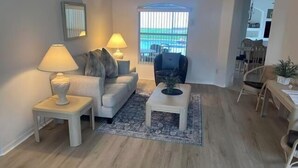 A living room with a sofa, two side tables with lamps, a coffee table, and a view through a window. - Orange Tree Pool Home with spa. Enjoy recreation and relaxation in this inviting community near the best of Orlando's hot spots! (Clermont)