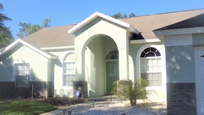 A two-story house with a light green exterior, a brown roof, and a front entrance with an arched doorway. - Orange Tree pool home features elegance, comfort, space and prime location! Book now! (Clermont)