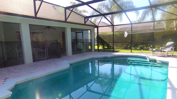 A swimming pool with a covered area, a patio with chairs, and a view of a lawn and trees. - Orange Tree pool home features elegance, comfort, space and prime location! Book now! (Clermont)
