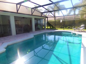 Une piscine dotée d’un espace couvert, une terrasse avec des chaises et une vue sur une pelouse et des arbres.