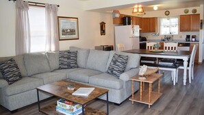 A living room with a grey sofa, a coffee table, and a dining area with a wooden table and chairs. - Pony Swim Ridge- Waterviews, Close to Memorial Park (Chincoteague)