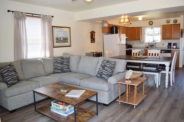 A living room with a grey sofa, a coffee table, and a dining area with a wooden table and chairs.