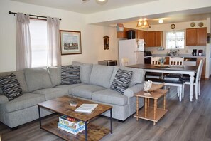 A living room with a grey sofa, a coffee table, and a dining area with a wooden table and chairs.