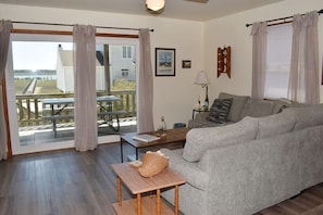 A living room with a grey sofa, a wooden coffee table, a lamp, and a view of a dock and water outside.