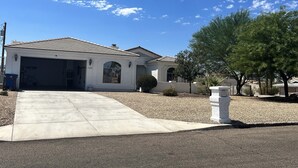 A single-story house with a garage, a small patio, and a large tree in front. - Spacious, Clean, Family Friendly, Lake Havasu Home with Boat Deep Garage! (Lake Havasu City)