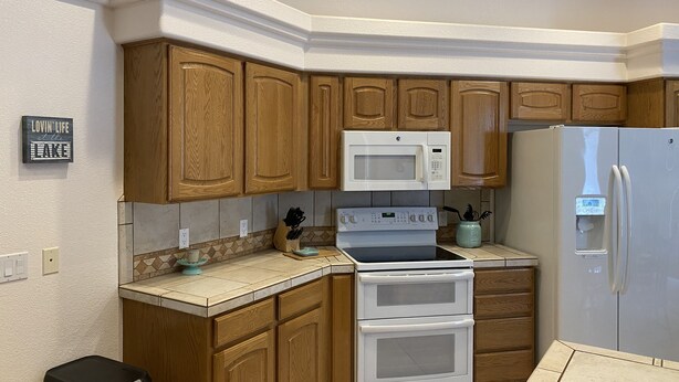A kitchen with wooden cabinets, a white stove, a microwave, and a refrigerator. - Spacious, Clean, Family Friendly, Lake Havasu Home with Boat Deep Garage! (Lake Havasu City)