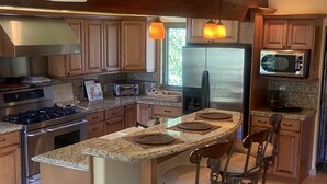 Una cucina moderna con piani in granito, elettrodomestici in acciaio inossidabile, mobili in legno e un'isola centrale con sgabelli da bar.