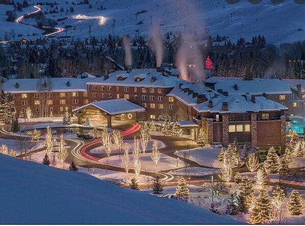 A snow-covered hotel with multiple buildings, a winding road, and a ski slope in the background.